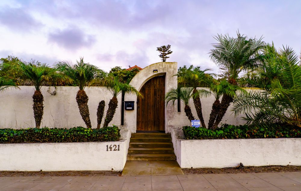 a adobe wall and door with palm trees in front