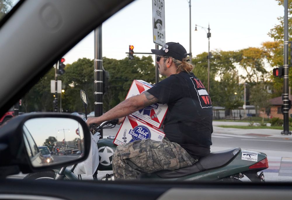 a guy on a motorcycle with 2 30 can cases of pbr on his lap