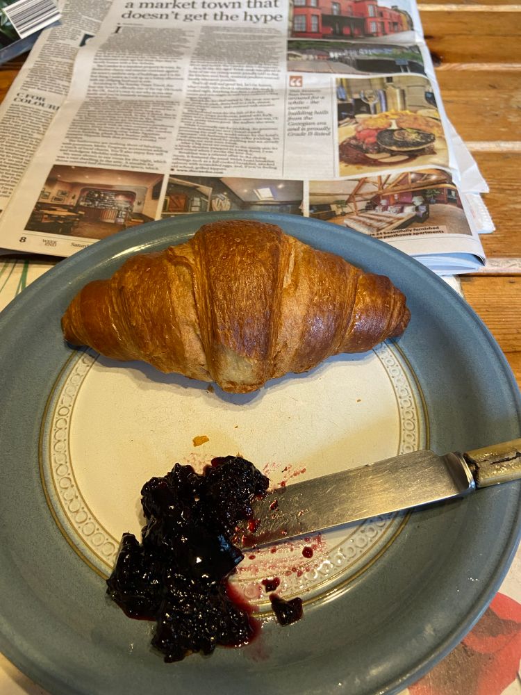 Croissant on a white plate with jam and knife