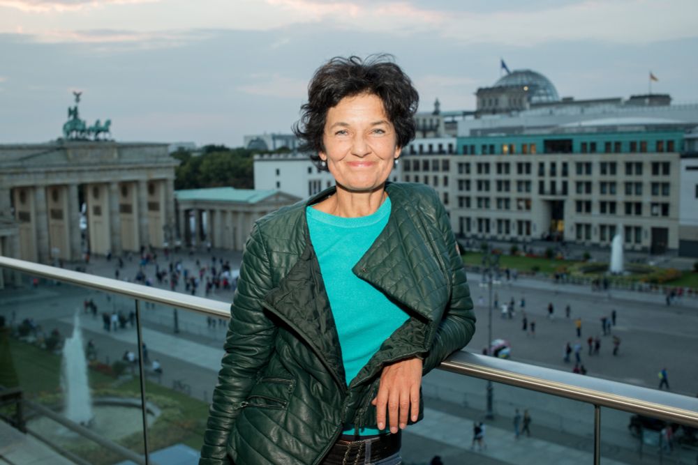 Ein Foto von Gerald Zörner zeigt Birgit Dahlke vor einem Balkongeländer stehend. Im Hintergrund ist der Parsier Platz in Berlin mit dem Brandenburger Tor zu sehen.