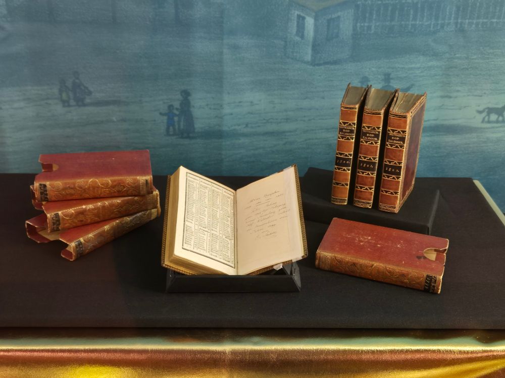 Bücher mit rotem Einband sind in einer Vitrine als Teil der Ausstellung zum GOTHA um ein geöffnetes Exemplar angeordnet. Es handelt sich um Exemplare des Gothaischen Hofkalenders aus der Zeit um 1800.