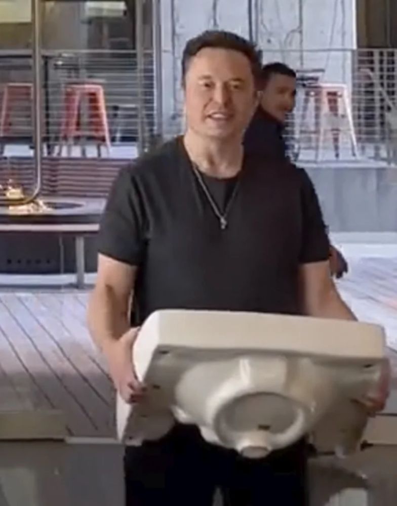 Elon performing a lame joke by holding sink and saying “let that sink in.”