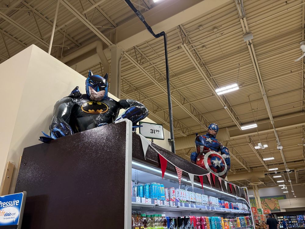 Oddly inflated Batman and Captain America on top of a drink fridge
