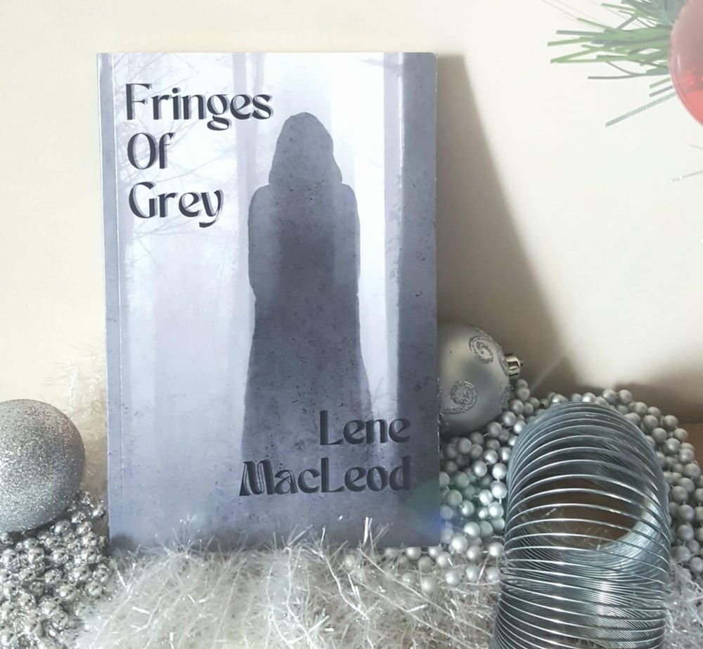 Book Fringes of Grey by Lene MacLeod displayed with silver-coloured props of Christmas baubles.