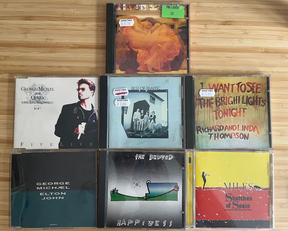 A selection of budget CDs on a table: Malcolm McLaren and the Bootzilla Orchestra's Waltz Darling, George Michael and Queen's Five Live, Traffic's Best Of Traffic, Richard and Linda Thompson's I Want To See The Bright Lights Tonight, George Michael and Elton John's Don't Let The Sun Go Down On Me, The Beloved's Happiness and Miles Davis's Sketches Of Spain.