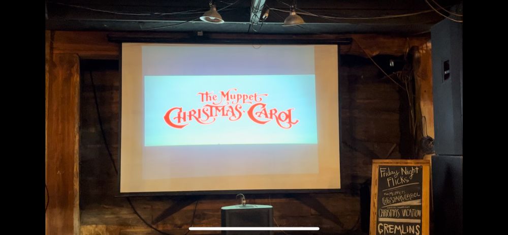 The title card for The Muppet Christmas Carol on a projection screen outside a bar.