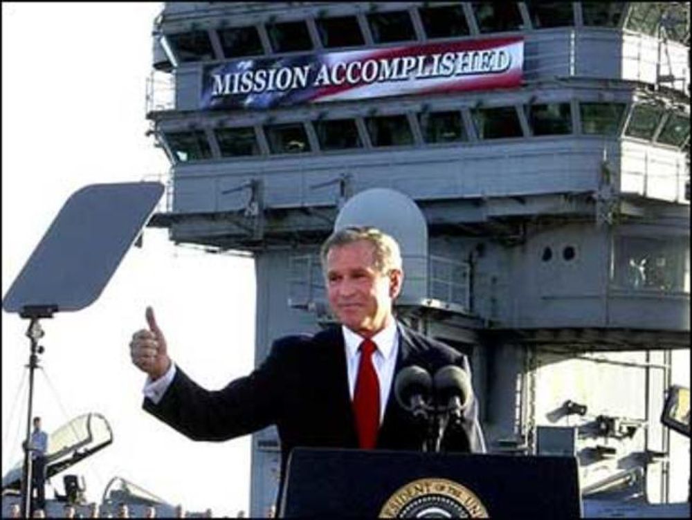 George W. Bush famous photo op on an aircraft carrier, 'Merica-style banner says "Mission Accomplished" behind him. Graphic design was clearly someone's passion.