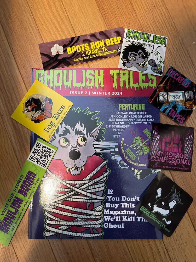 The winter 2024 issue of Ghoulish Tales, surrounded by an assortment of Ghoulish stickers and bookmarks