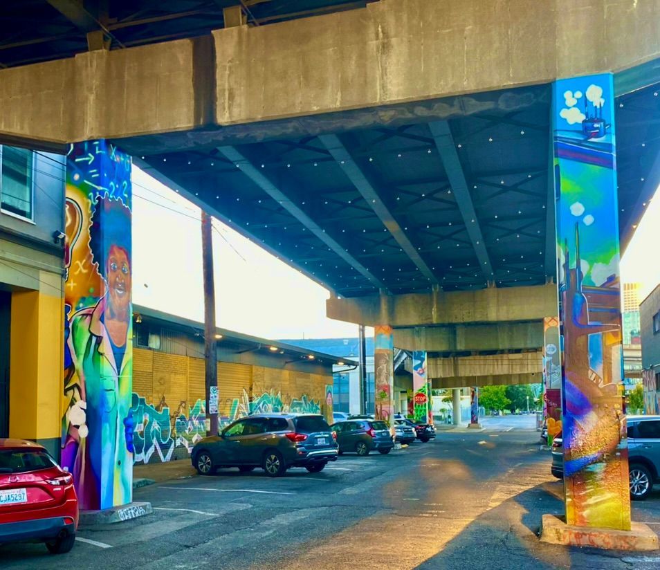 under the overpass in industrial inner SE, cars parked by columns & walls covered in graffiti on a hot summer evening