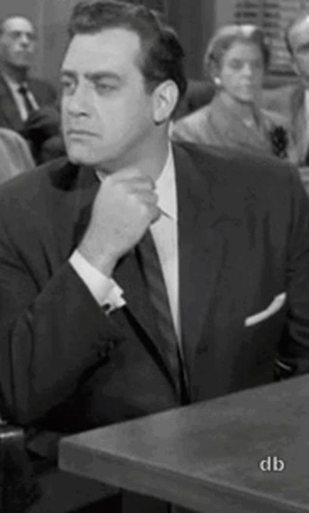 a man in a suit and tie is sitting at a table with his hand on his neck .