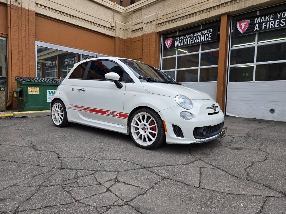 A white Fiat 500 Abarth in front of a Firestone Auto Center