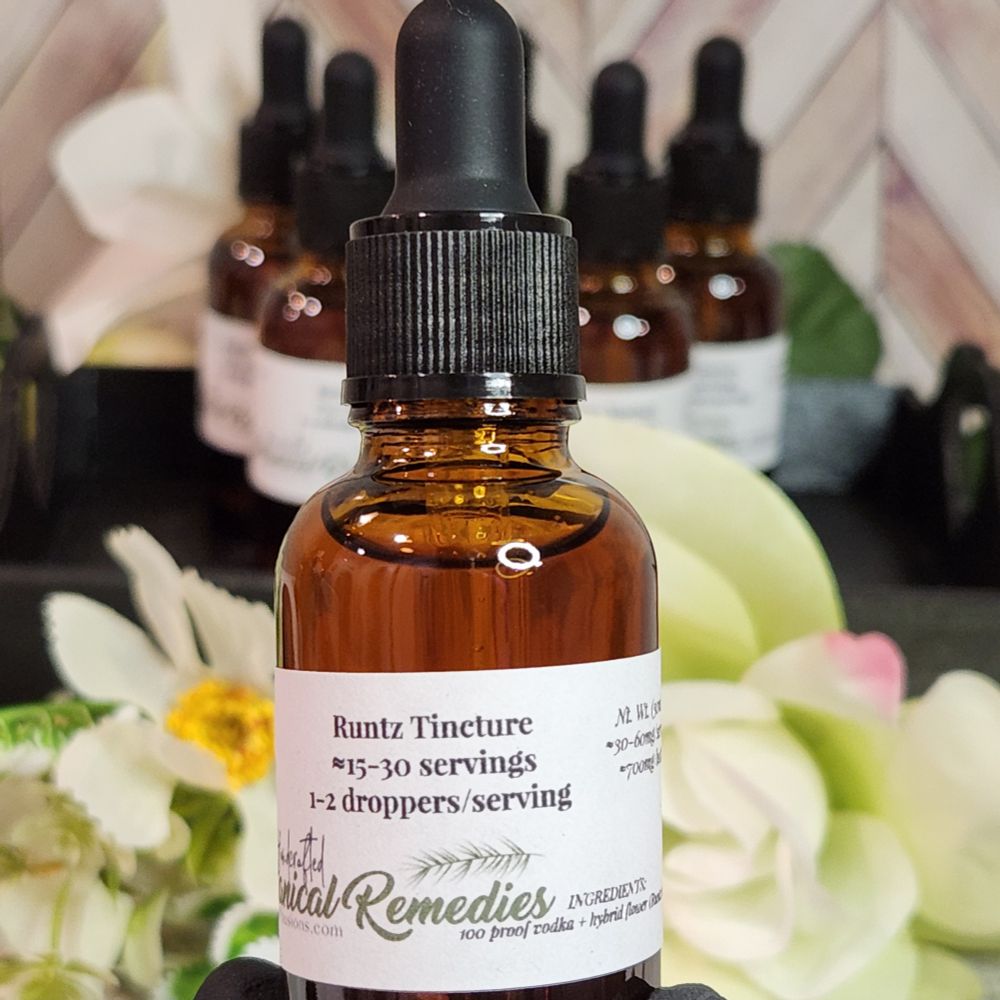 A close-up of a single amber glass dropper bottle labeled "Runtz Tincture" in focus, with additional bottles and artificial flowers blurred in the background. The label mentions serving size and ingredients, including 100 proof vodka and hybrid base distillate.