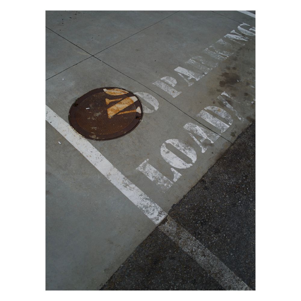 Photo of a parking lot with a manhole cover with the words “no parking” and “loading” painted