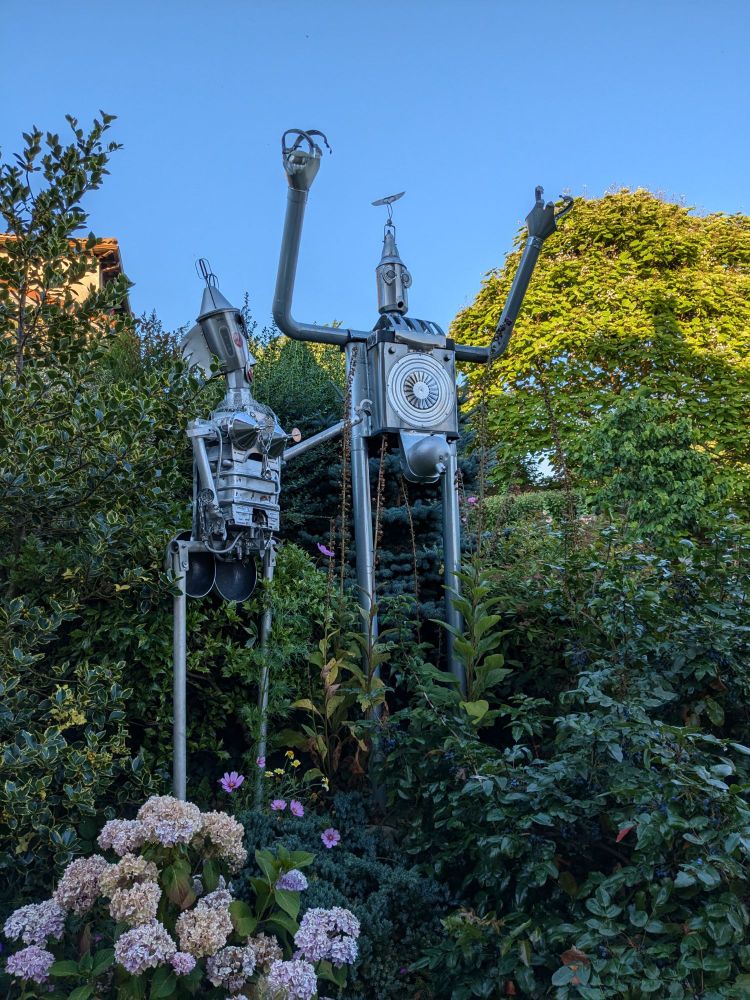 Dos esculturas de robots de metal en un jardín. 