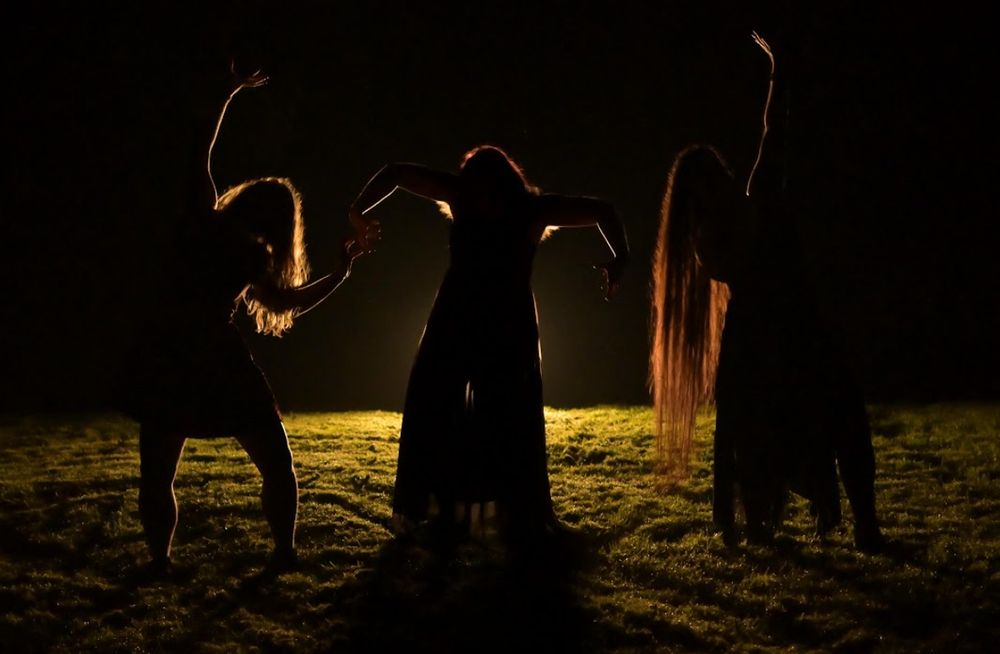 A photograph of three women being back-lit and taking stances to mimic witches.