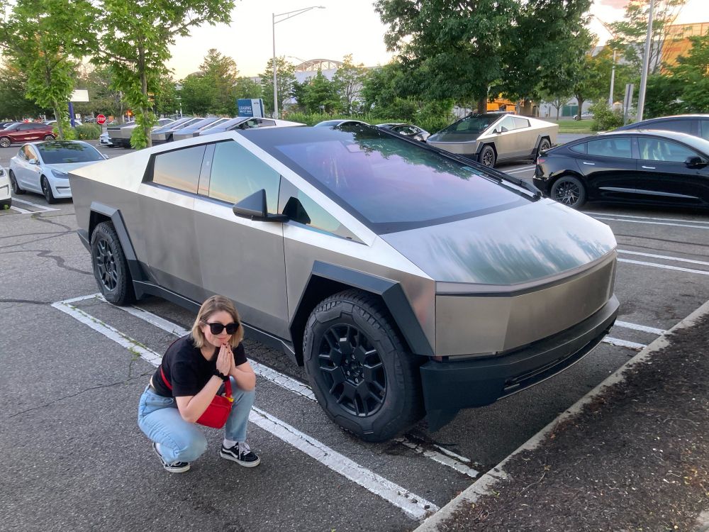 me, crouched and praying ironically infront of a ridiculous-looking “cybertruck” in a car park