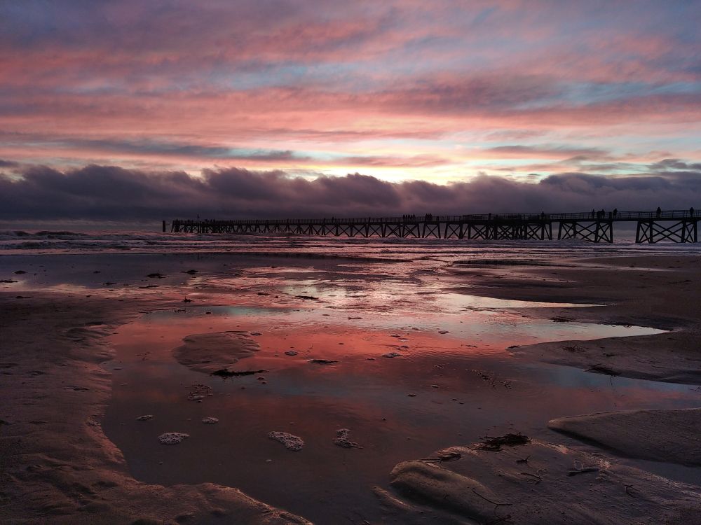 Soleil couchant derrière des nuages de traîne se reflétant sur le sable à marée montante 
