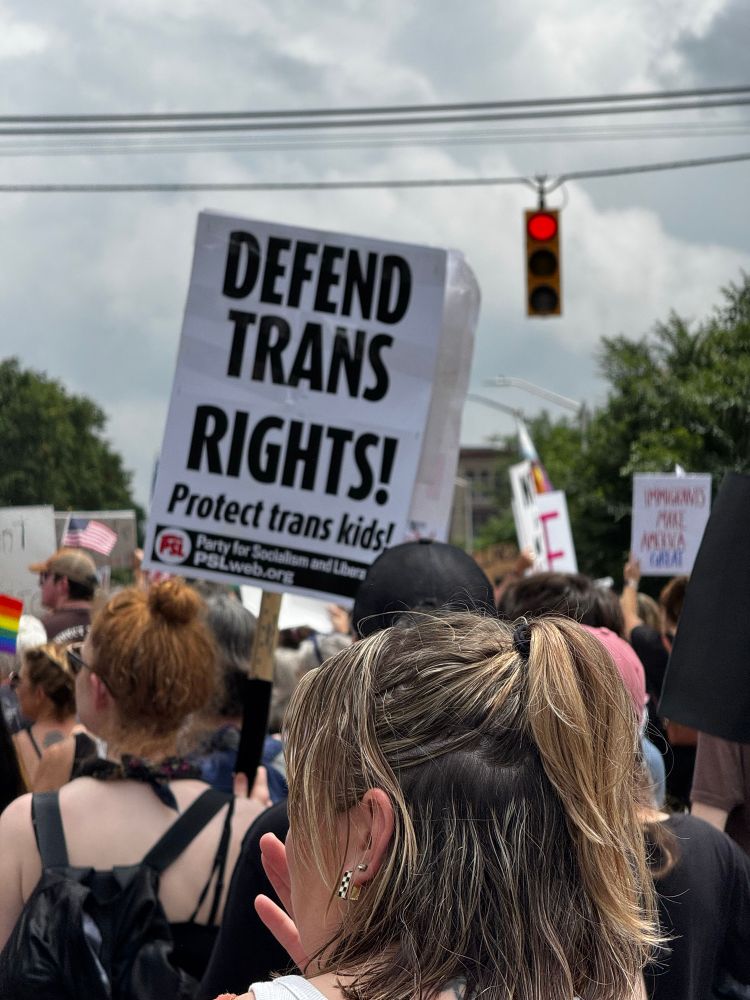 Protesters hold a sign “defend trans rights”