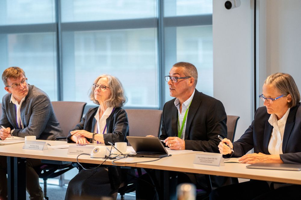 image of four people sat at a table in suits. One person is speaking