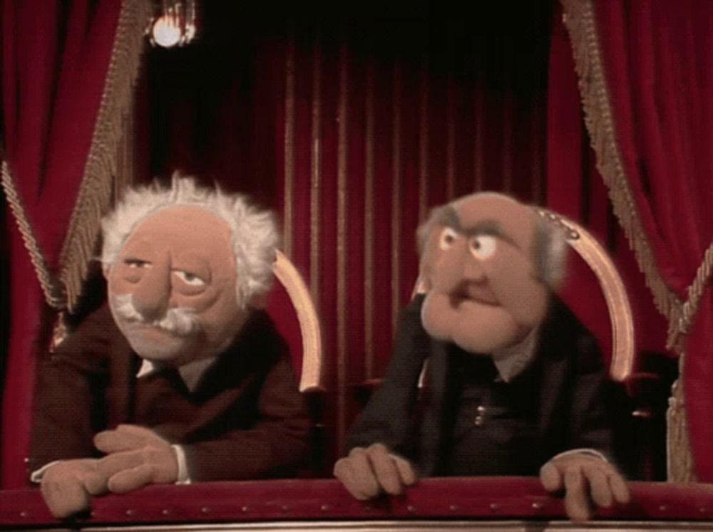 two muppets are sitting in front of a red curtain in a theatre