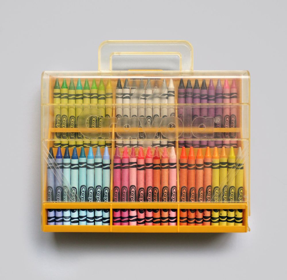 A yellow plastic suitcase with a clear front that has a frosted Crayola logo across the front. Inside are 96 wax crayons arranged chromatically. 