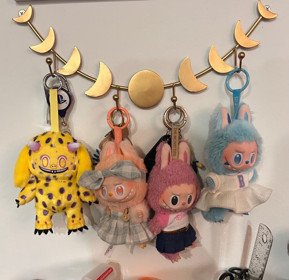 4 bag charms hanging from a key rack. 3 of them are traditional Labubus and 1 is the Spencer bag charm from dropout.tv