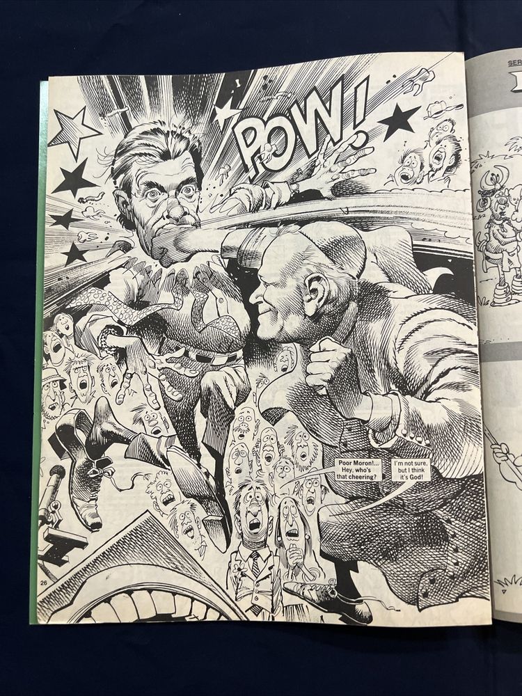 a super-dynamic full-page illustration of "Moron Downer Jr." getting a haymaker right in the chops (with accompanying POW!) from His Holiness Pope John Paul II, who looks pretty pleased with himself. A bunch of audience members look in in the background with shock. A man asks: "Poor Moron!... Hey, who's that cheering?" A woman standing next to him replies "I'm not sure, but I think it's God!"