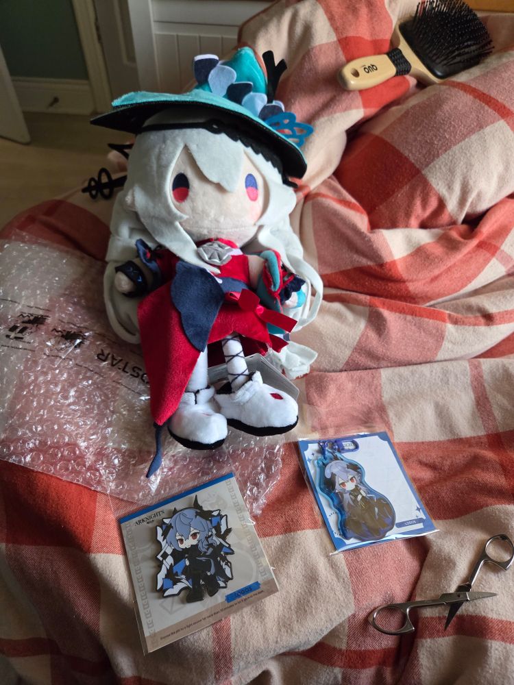 The top is a Skadi the Corrupting Heart plush, on the lower left is a glow in the dark Logos pin, and lower right is a Logos Keychain 