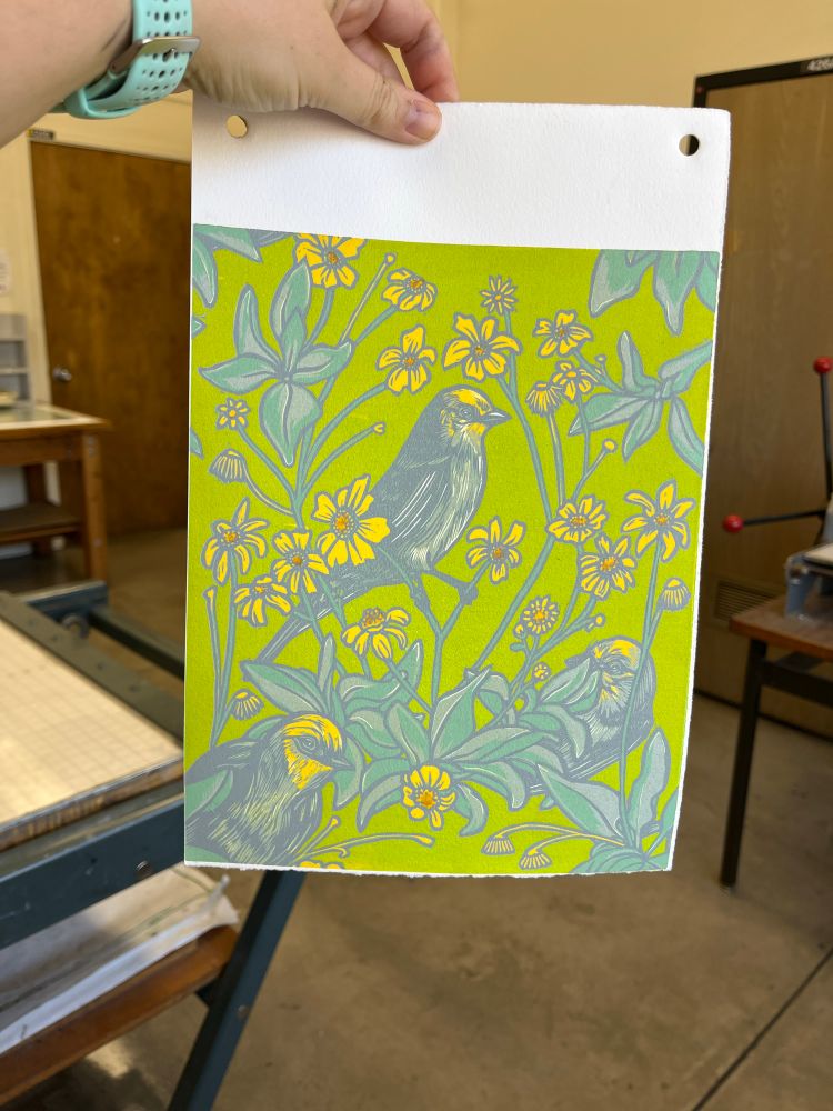 Hand holding a partially finished linocut print of birds and flowers 