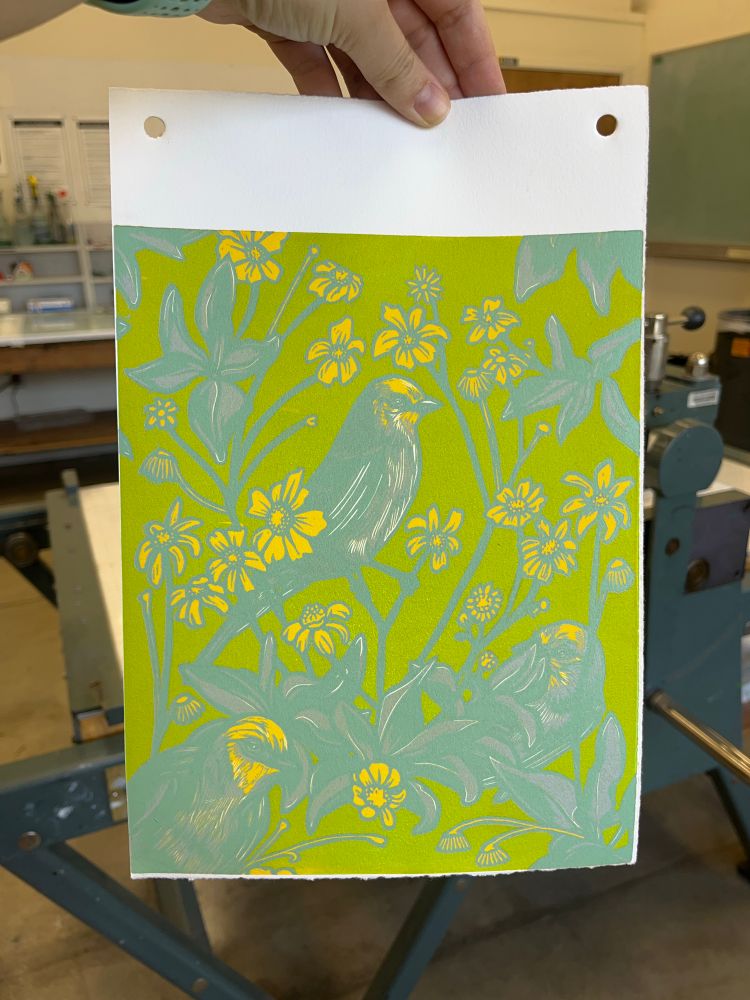 Hand holding a partially finished linocut print of birds and flowers 