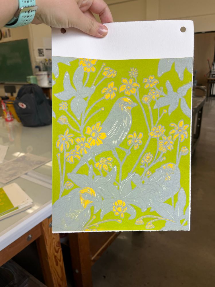 Hand holding a partially finished linocut print of birds and flowers 