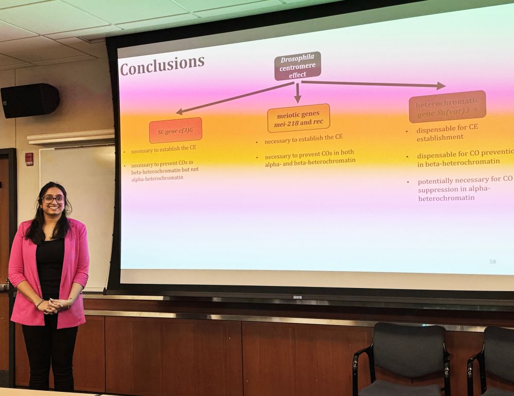 Photo of Nila Pazhayam next to screen showing her slide of the summary of the results of her research.