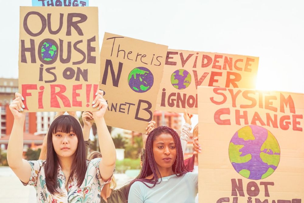 Protesters holding signs with climate change messages, including "Our house is on fire!" and "There is no Planet B," urging action.