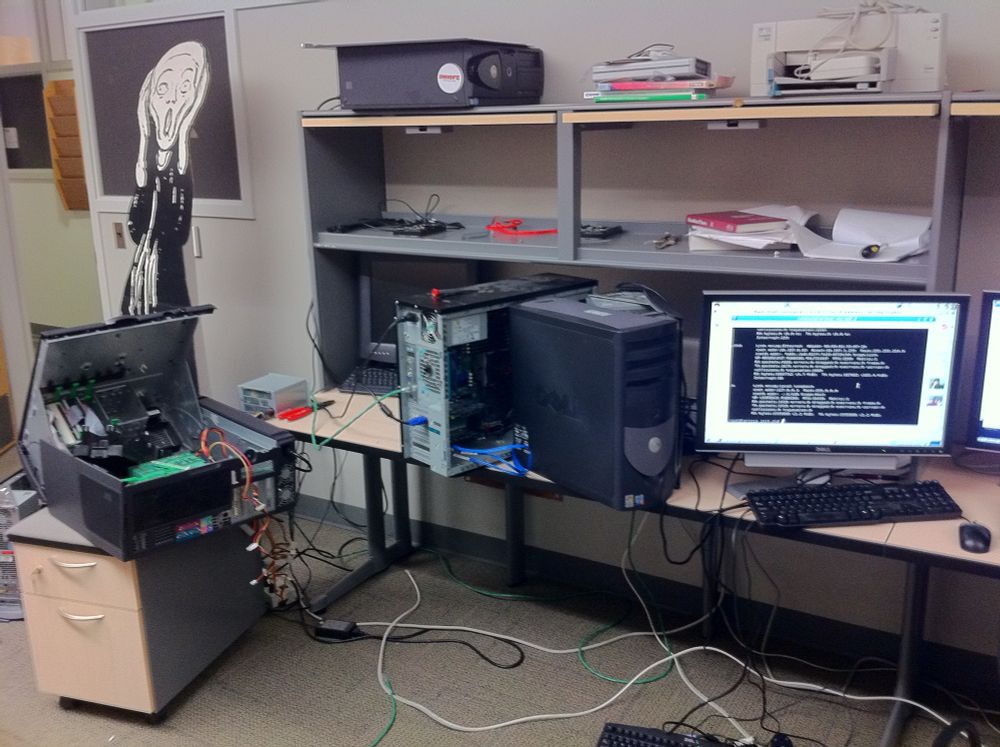 A cardboard cutout of the Scream character is next to three busted Linux boxes and a monitor. 