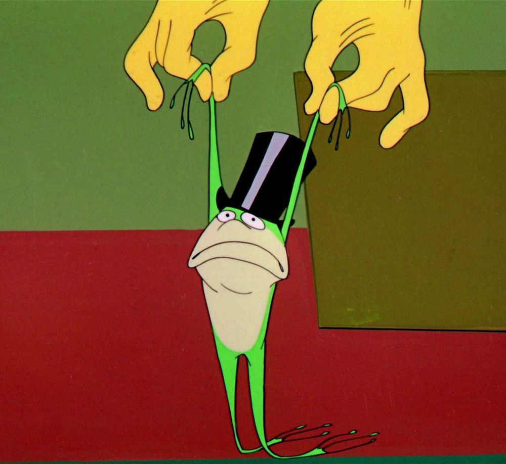 Michigan J. Frog, in real frog mode, looking gloomy as the construction worker holds him up by the wrists.