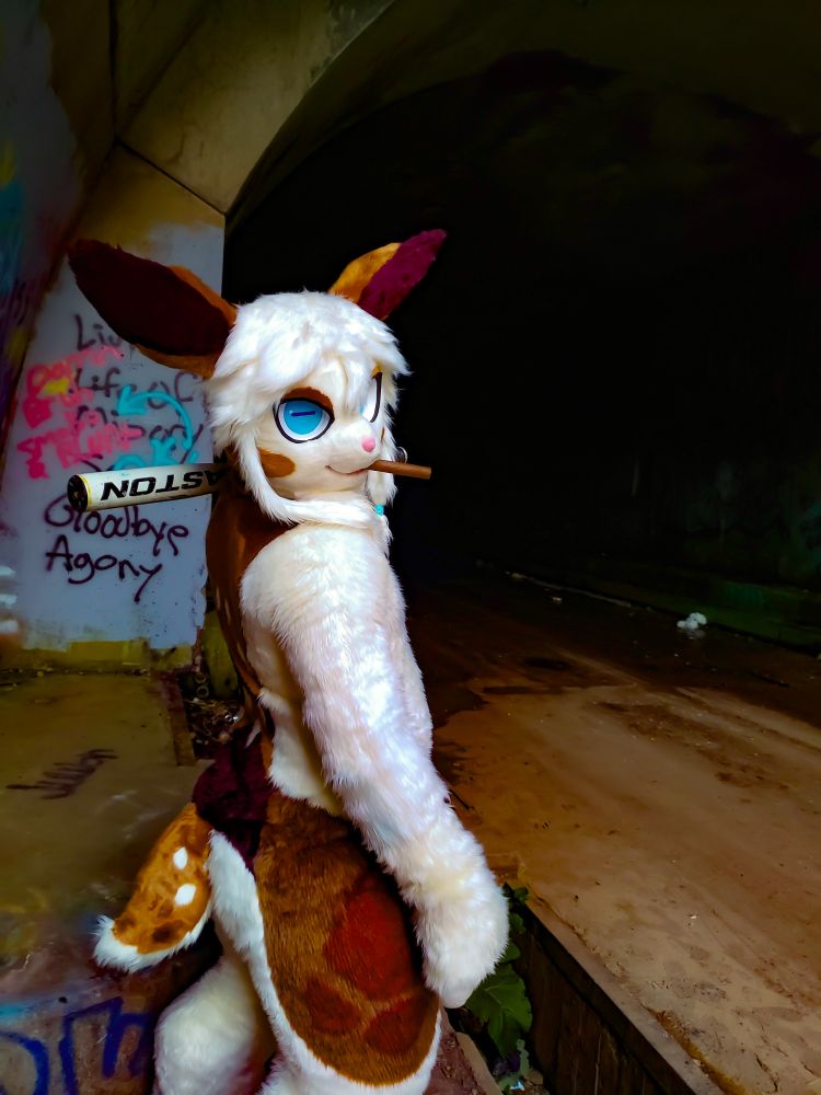 A white bipedal deer stands before a derelict concrete tunnel, looking at the camera. The deer is holding a baseball bat and has a large cigar in it's mouth.