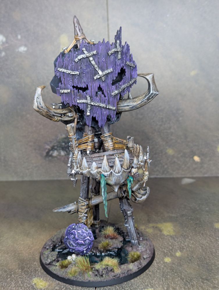 The Kruleboyz terrain piece from Games Workshop. It's a wooden tower with a swampy base. There's a crude wooden face at the top which is painted purple.