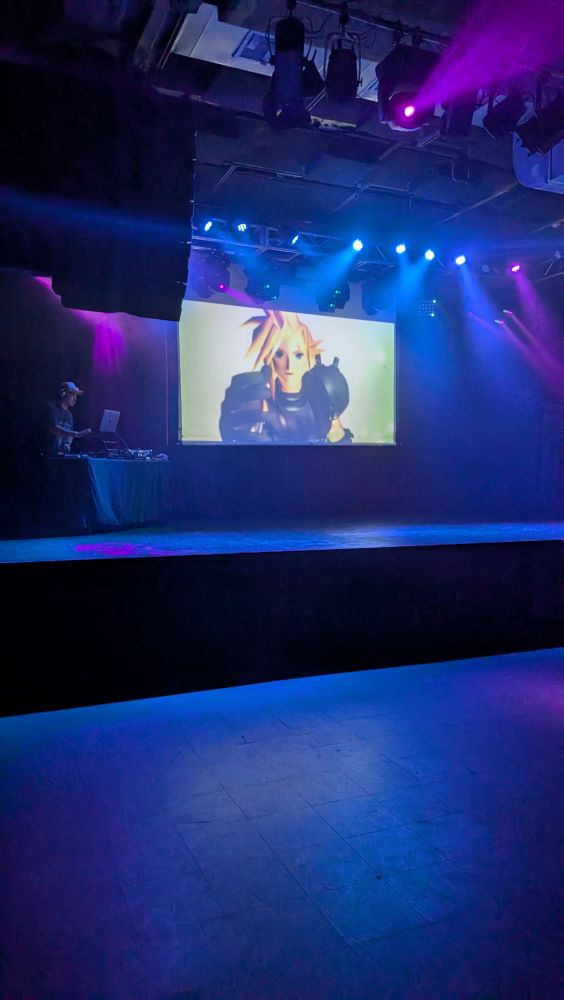 A stage with a screen playing a 3d cut scene from final fantasy 7 showing the main character, cloud.