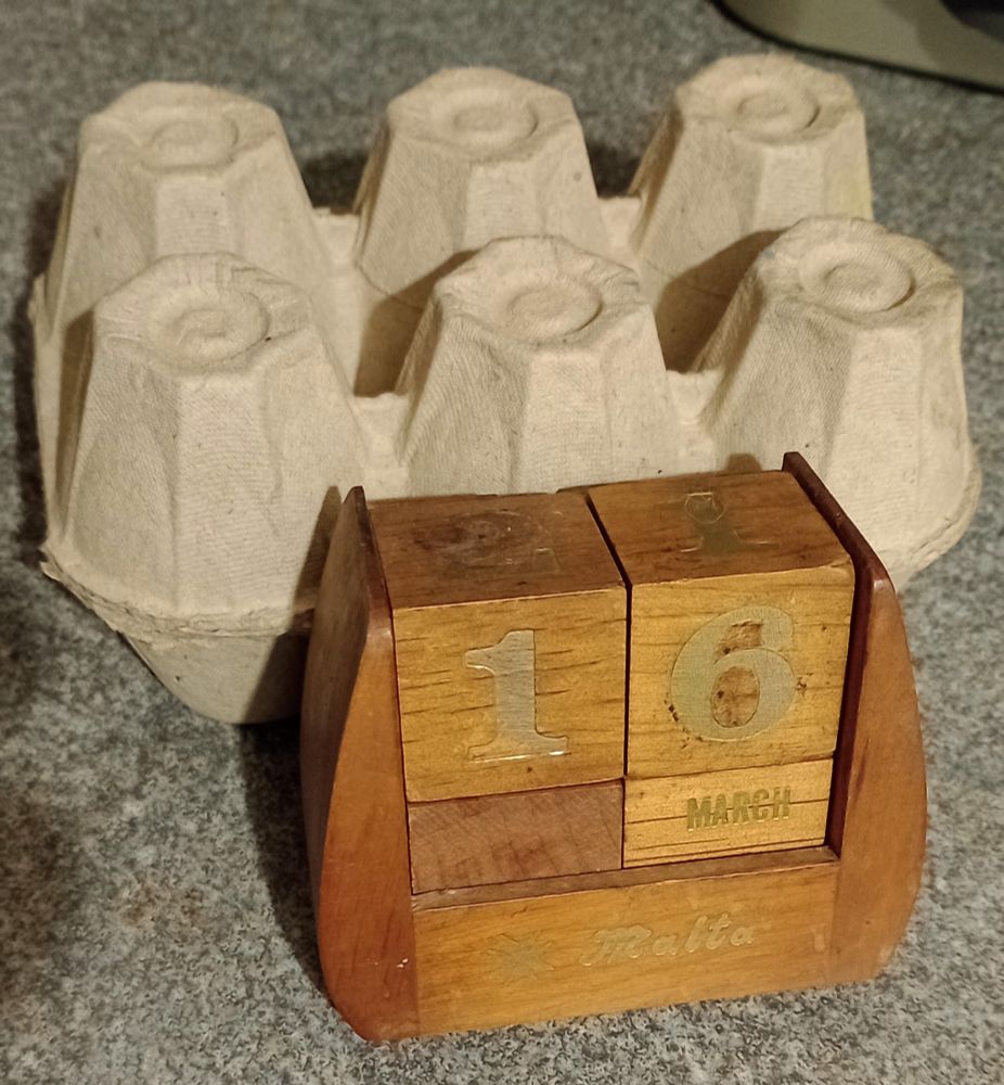 A wooden block based perpetual calendar in front of an eggbox