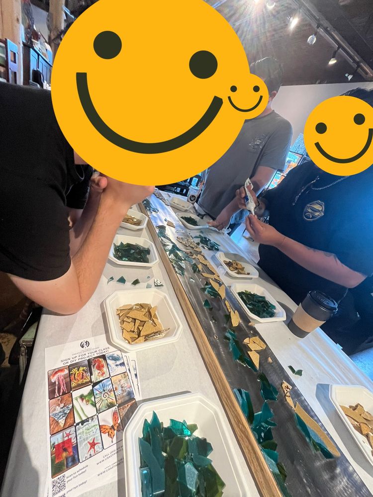 People standing at a table where there are bowls of cut glass and a long rectangle they are placing the glass on to represent water over sand. 