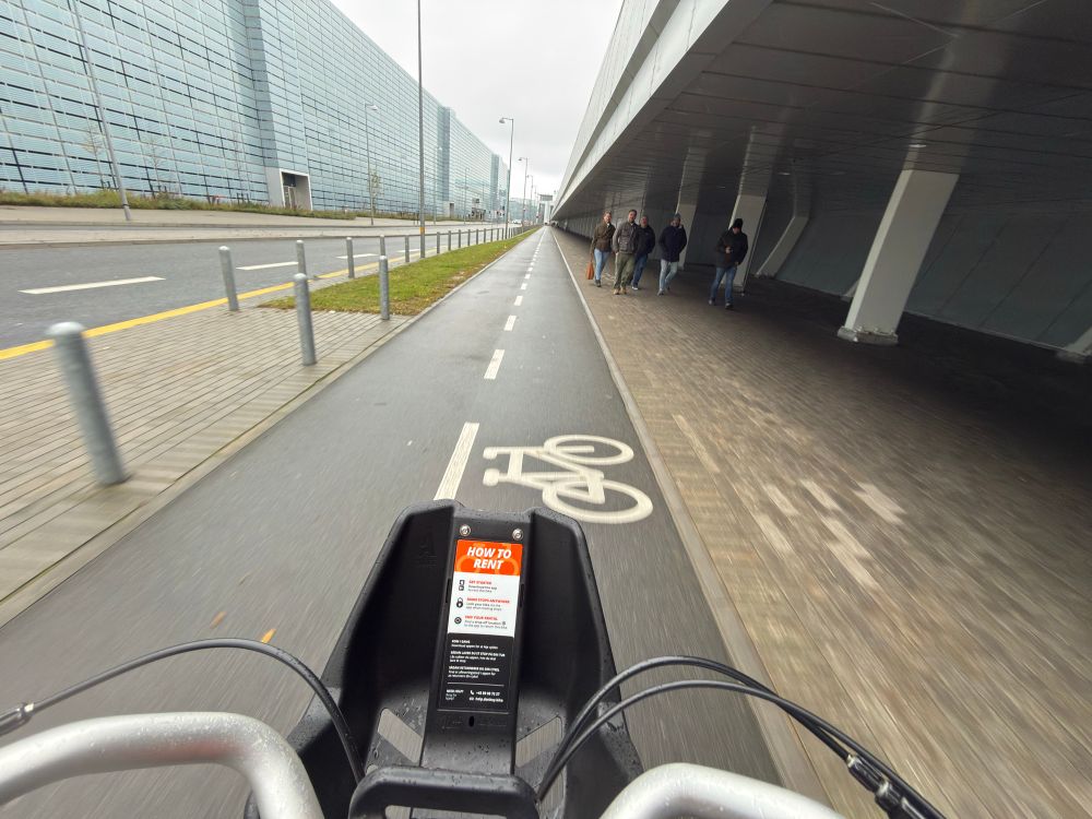 Handlebar shot next to airport buildings with cycle icon on cycleway. 