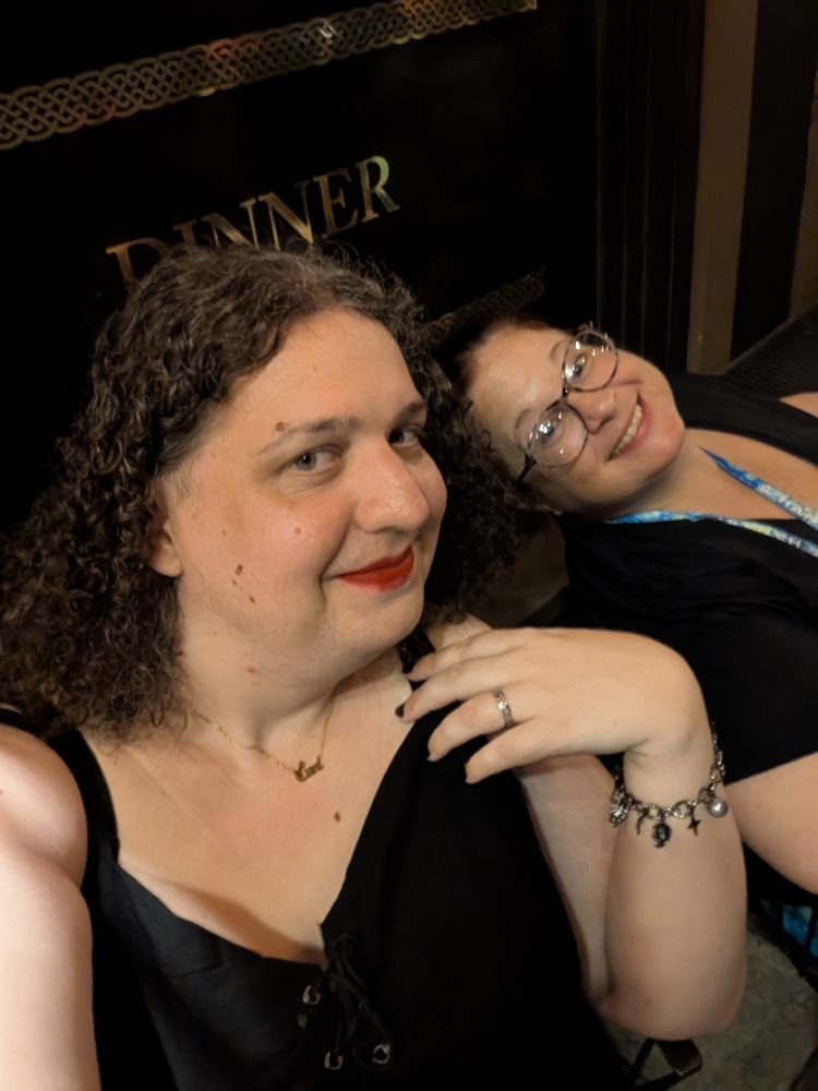 two women sit smiling and pose outside a bar