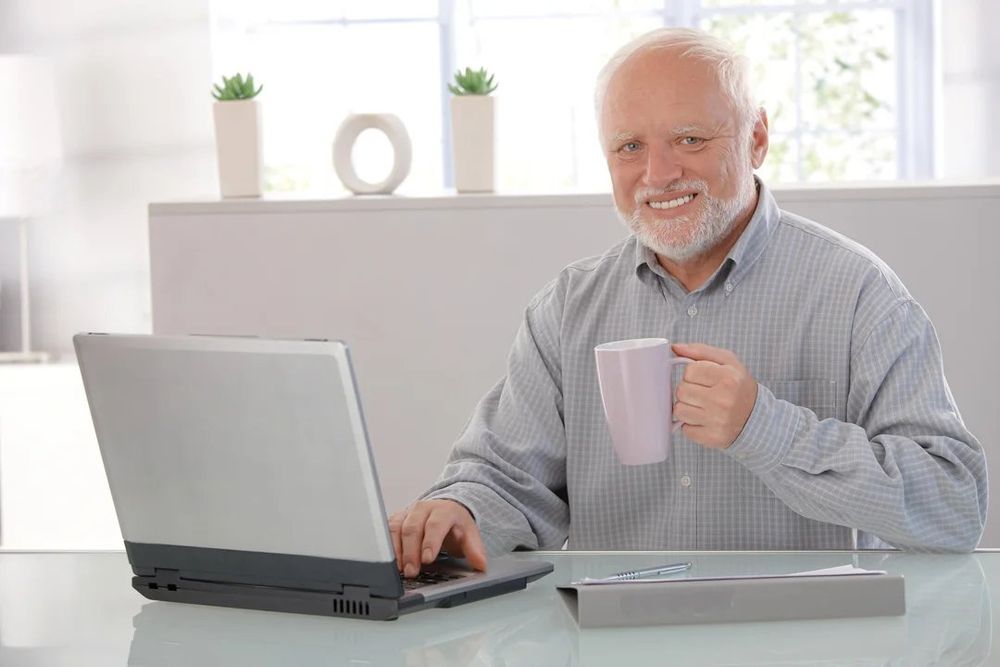 Hide the Pain Harold sitting in front of a laptop with a mug