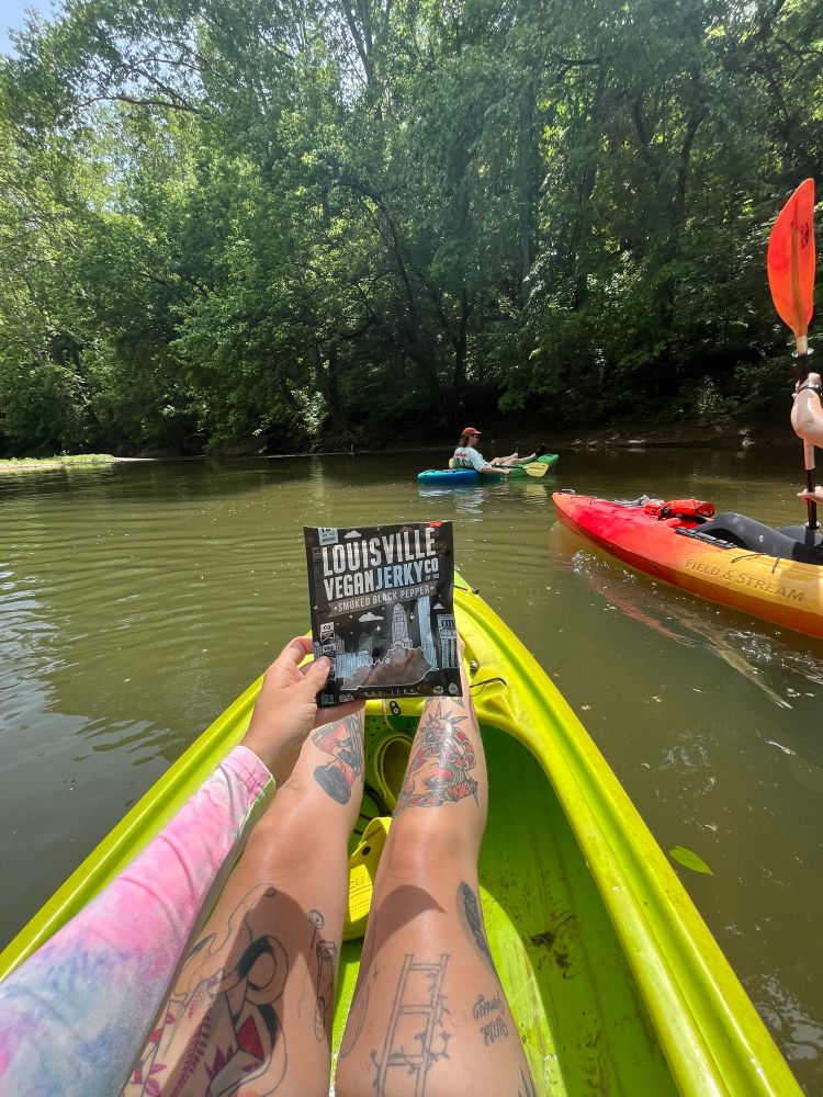 People in kayaks in a creek. The person taking the photo is holding a bag of vegan jerky. 