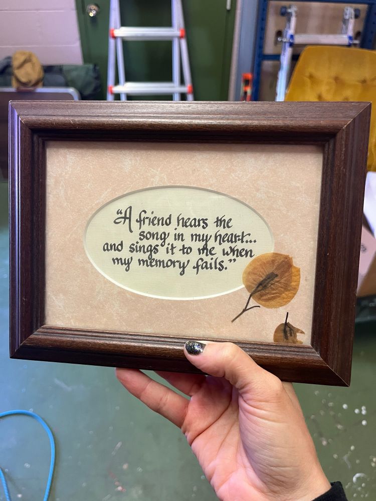 Wooden frame with calligraphy that says “a friend hears the song in my heart…and sings it to me when my memory fails” with dried seed pods in the corner. 