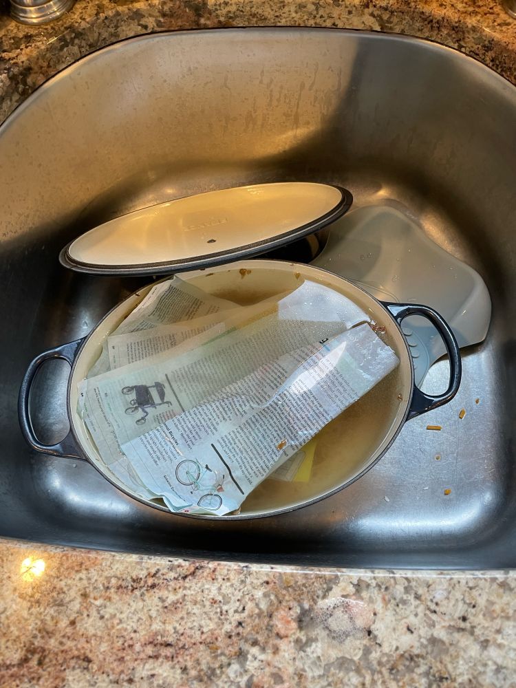 A Dutch oven in the sink with torn magazines floating in water inside