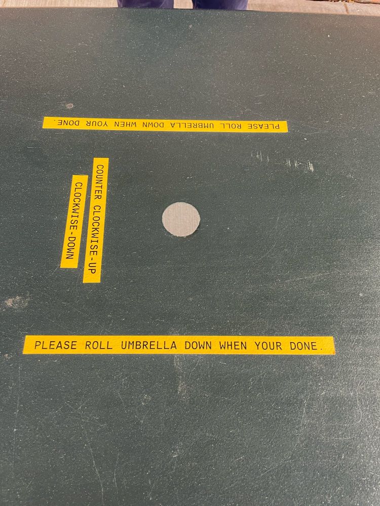 A table with a hole and a label “Please roll umbrella down when your done” the your is misspelled