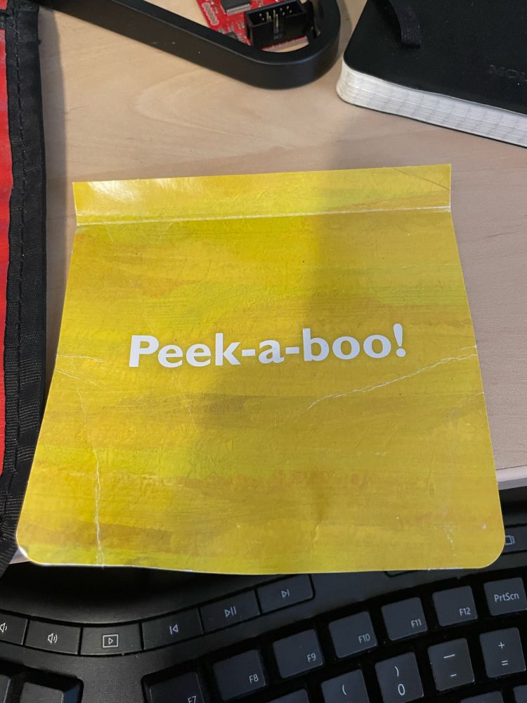 A yellow piece of paper from a children book that says “peek-a-boo!”