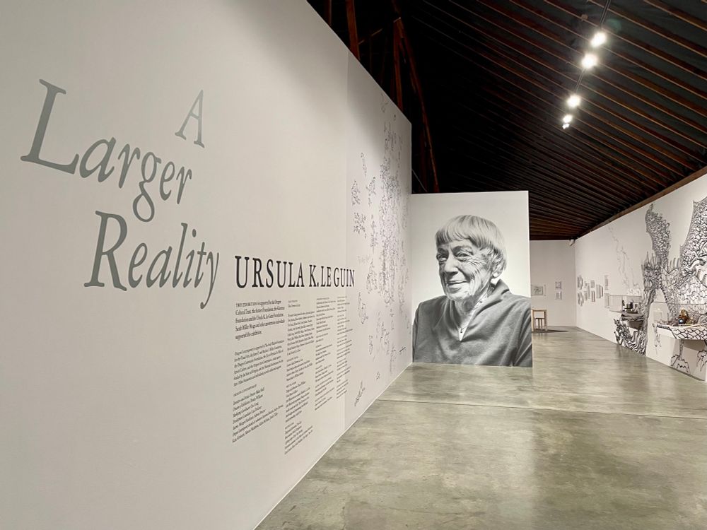 A Larger Reality: Ursula K. Le Guin, with wall-sized Earthsea map, grinning photo of Ursula by William Anthony, and dragon mural by Ursula Barton