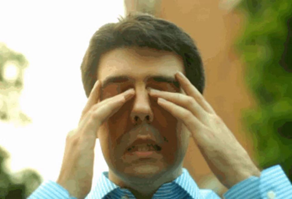 a man in a blue and white striped shirt is rubbing his eyes with his hands